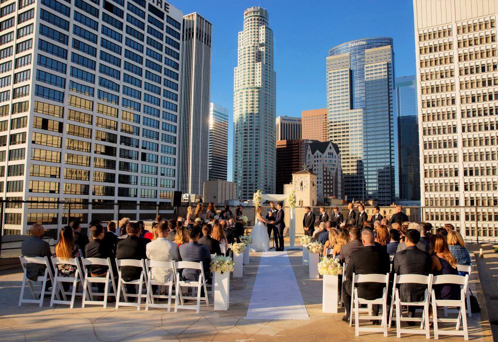 A wedding ceremony at the Los Angeles athletic club is taking place on a rooftop with a city skyline in the background