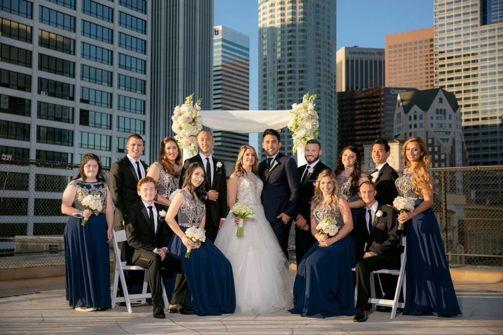 A bride and groom are posing for a picture with their wedding party in front of a city skyline.
