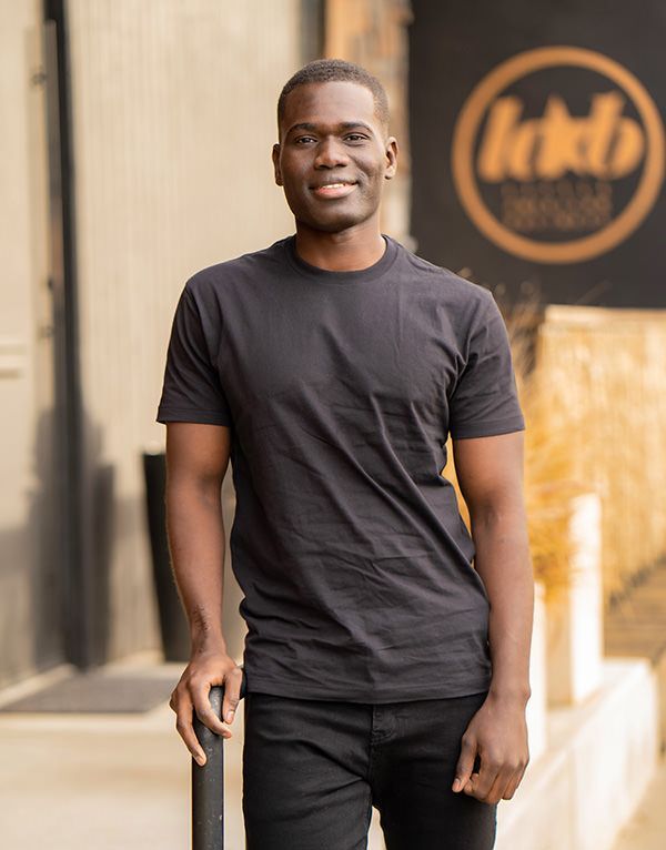 A man in a black t-shirt is smiling for a a dating photo.