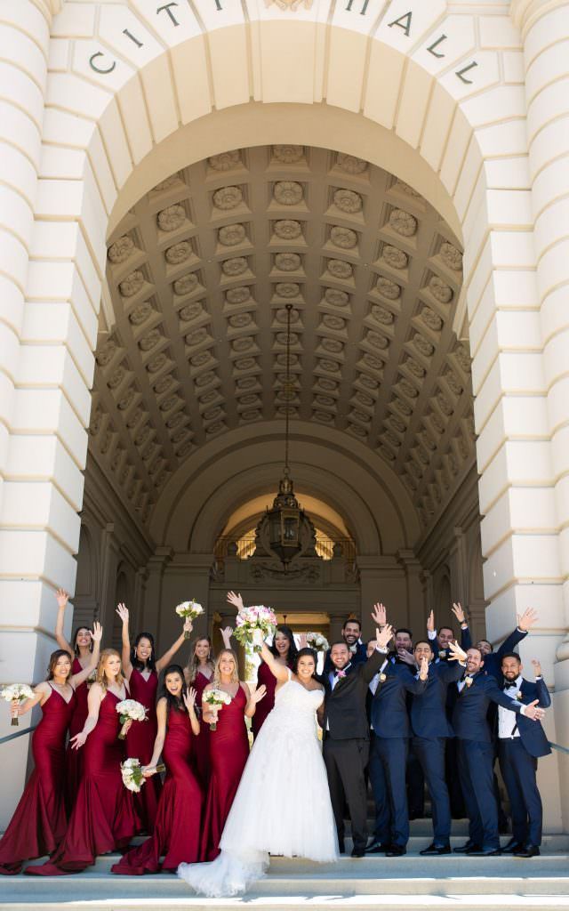 A bride and groom pose with their wedding party in front of the Pasadena city hall