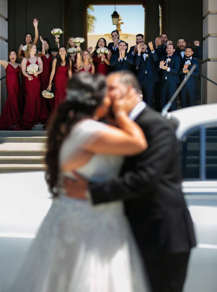 A bride and groom kiss in front of their wedding party