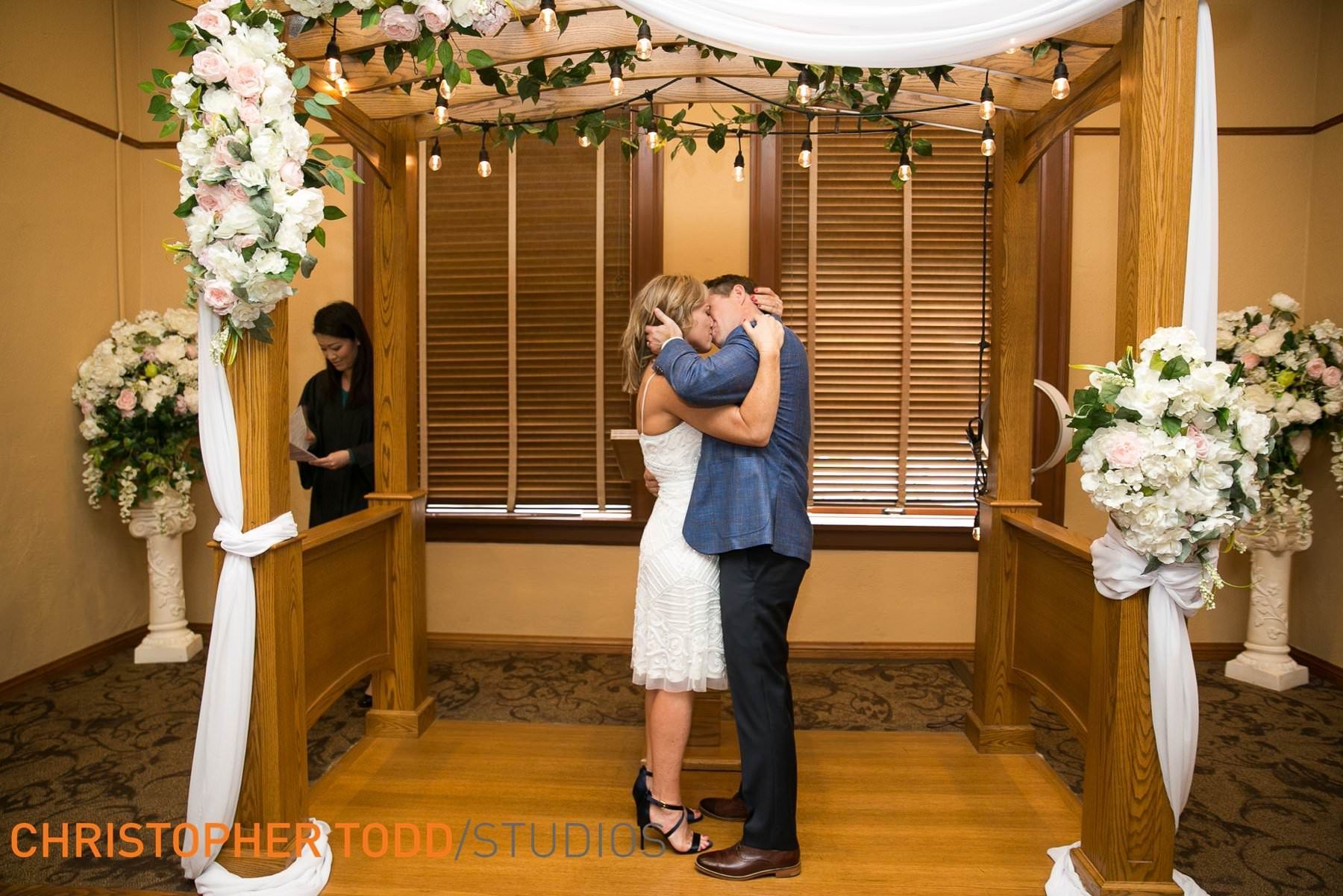 A bride and groom are kissing under a canopy at their wedding ceremony.