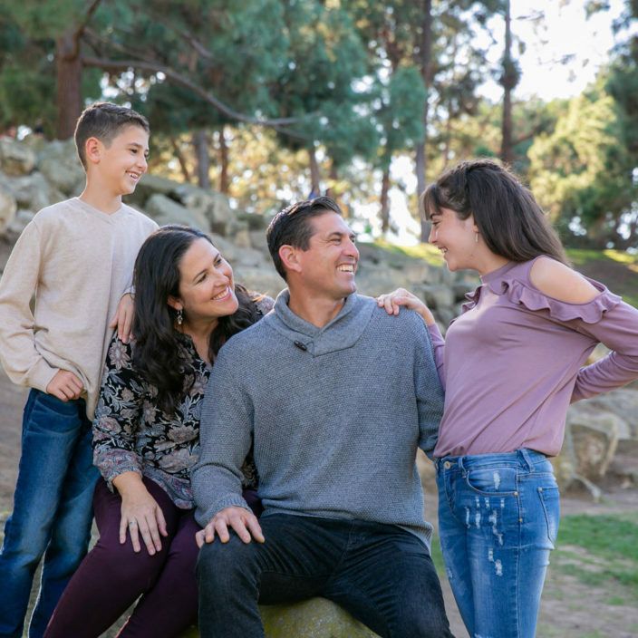 A family is posing for a picture while sitting on a rock in Costa Mesa Park.