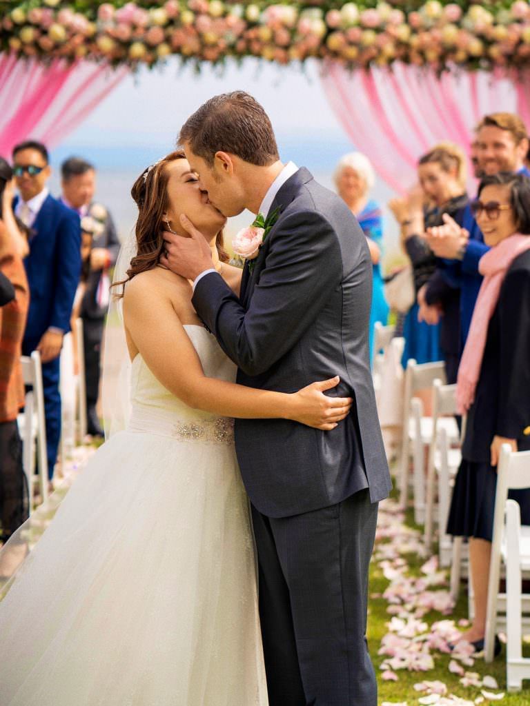 A bride and groom are kissing at their wedding ceremony.