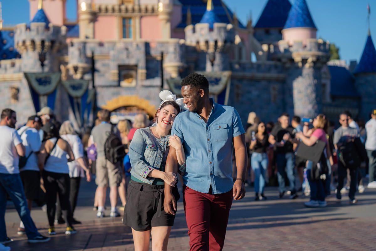 Disneyland Engagement Photographer A man and a woman are walking in front of a castle at Disneyland.
