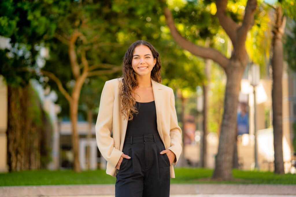 A woman is standing on a sidewalk with her hands in her pockets.