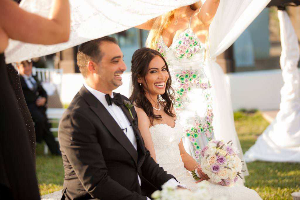 A Persian bride and groom are sitting under a white cloth during their wedding ceremony