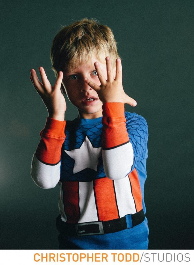 A young boy in a captain america costume covering his face with his hands