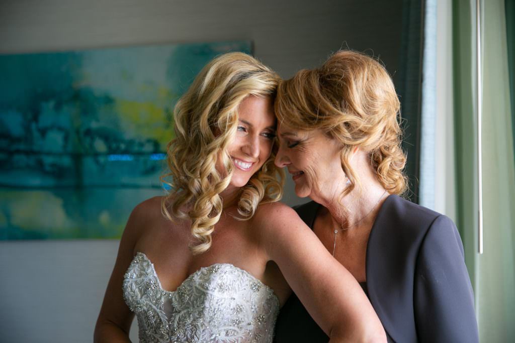 A bride and her mother are standing next to each other in front of a window.