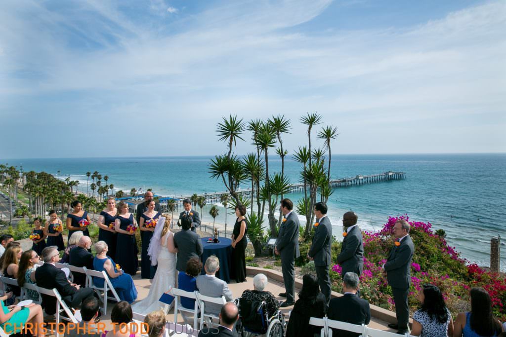 A wedding ceremony is taking place on a cliff overlooking the ocean