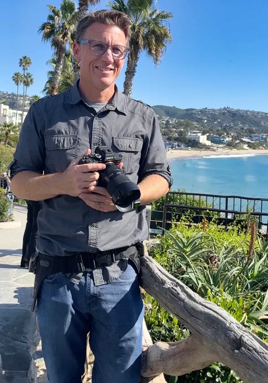A man is holding a camera in front of a beach.