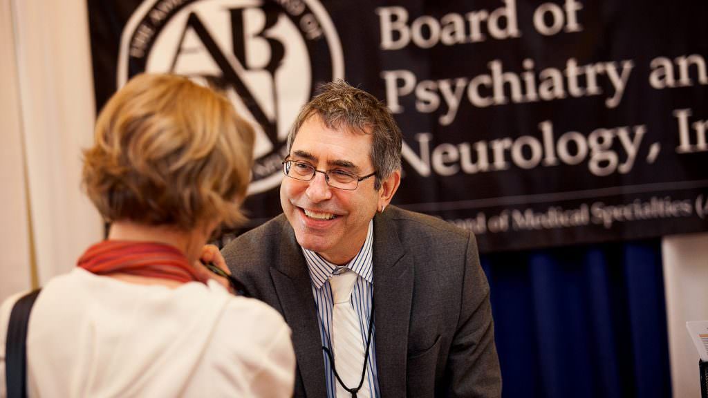A man and woman are talking in front of a sign that says board of psychiatry and neurology