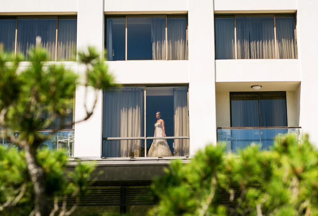 A bride in a wedding dress is standing on a balcony of a hotel.