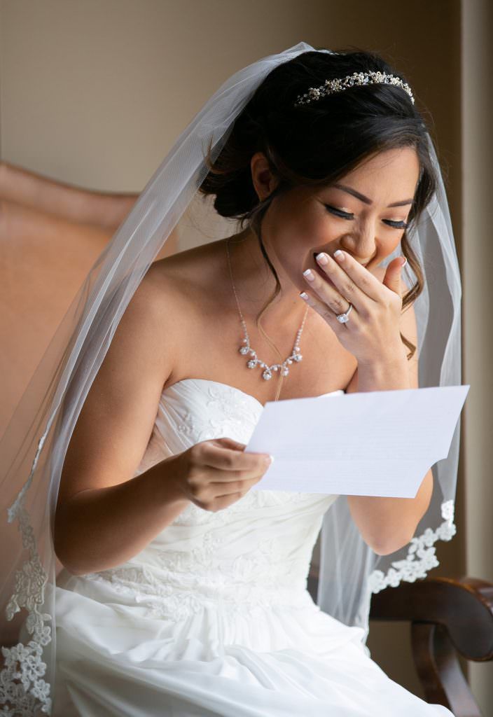 A bride in a wedding dress is reading a letter from her groom.