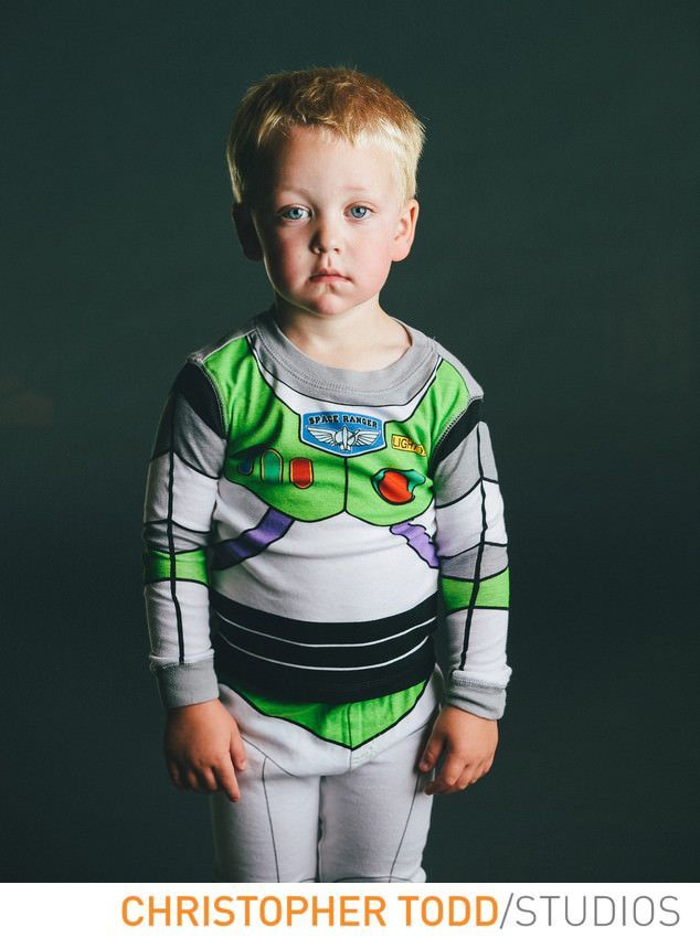 A young boy in a buzz lightyear costume is standing in front of a black background.