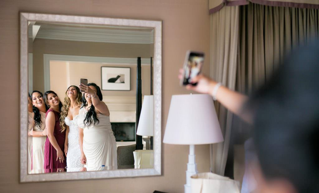 A woman is taking a picture of her bridesmaids in front of a mirror.