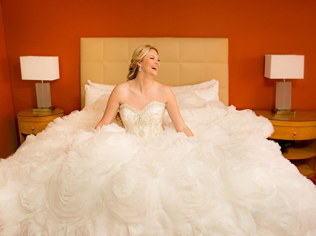 A bride in a wedding dress is sitting on a bed at the Irvine Hyatt hotel.