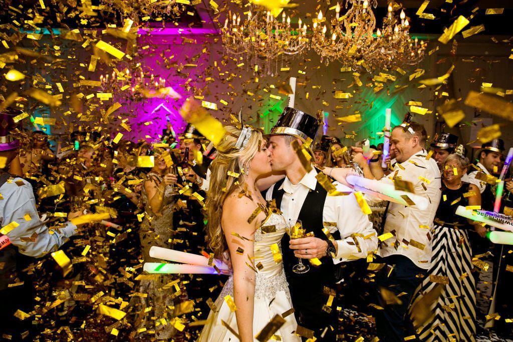 A bride and groom kissing in front of a crowd of people at a new year 's eve party.