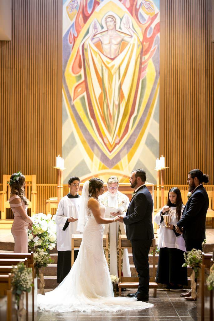 A bride and groom are holding hands during their wedding ceremony in a church.