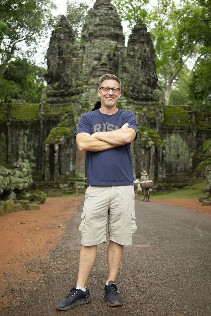 Christopher Toddis is standing in front of a temple in Siem Reap with his arms crossed.