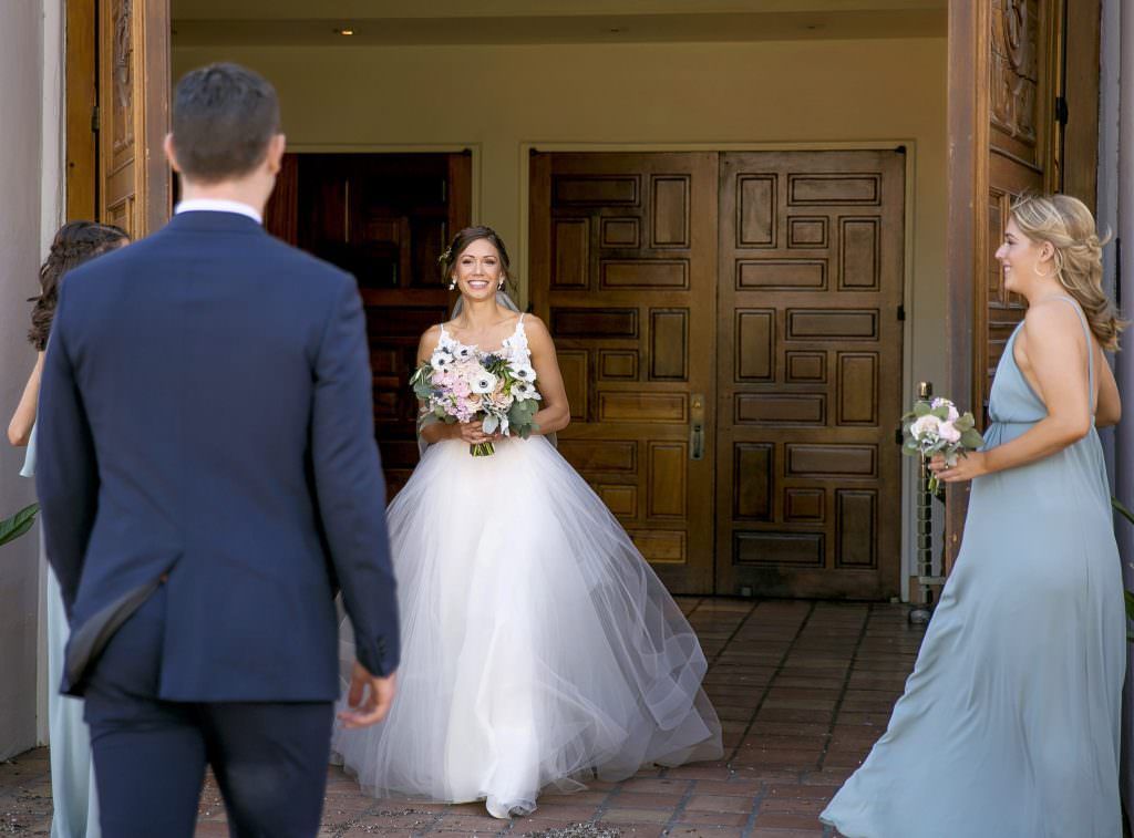 A bride and groom are walking out of a church with their bridesmaids.