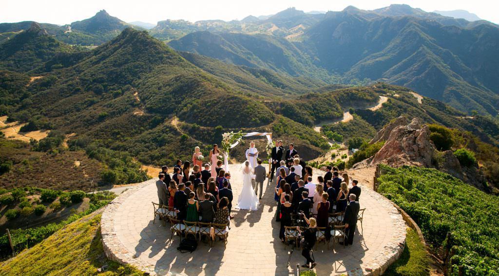 A wedding ceremony is taking place on top of a mountain helicopter pad at Malibu Rocky Oaks estates. 