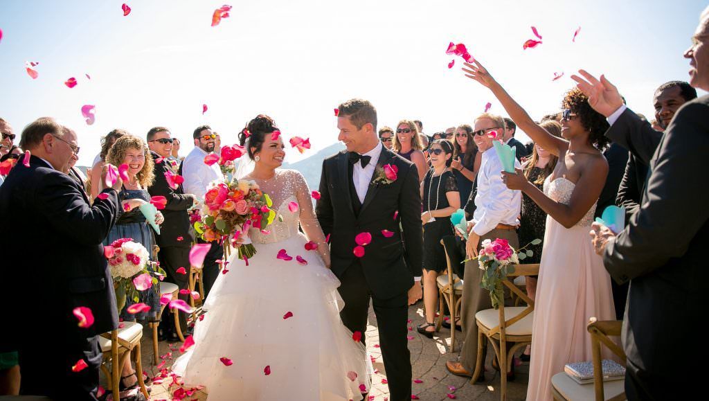 A bride and groom are walking down the aisle surrounded by flower petals