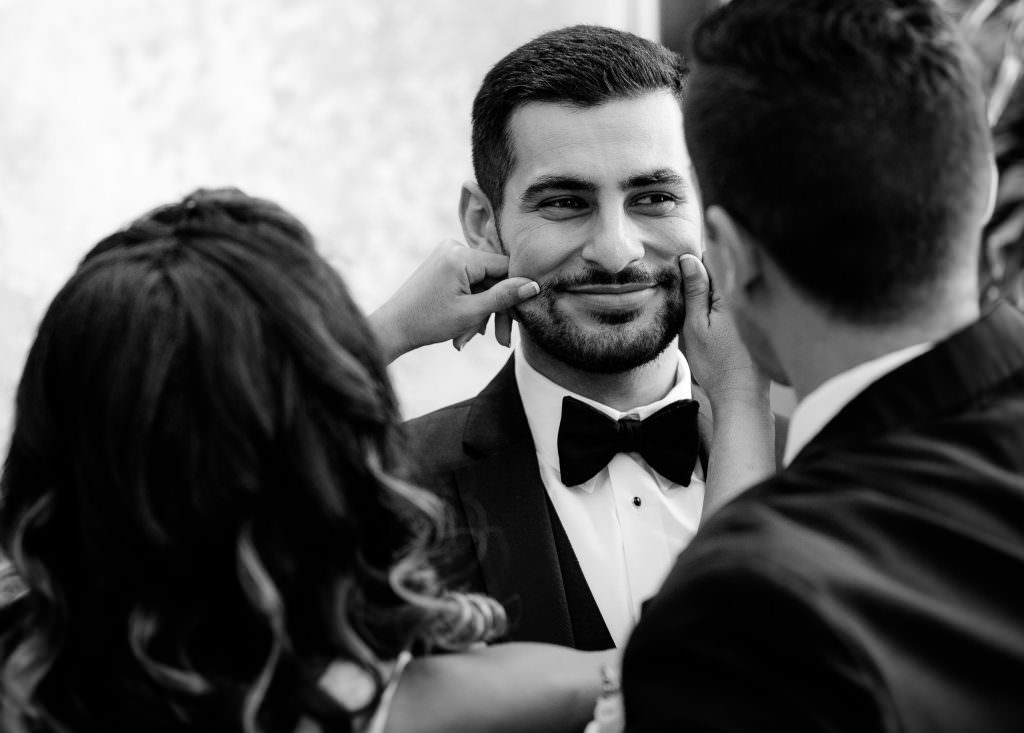 A man in a tuxedo and bow tie is being touched by a woman in a black and white photo.