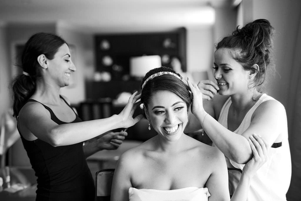 A bride is getting her hair done by two women in a black and white photo.
