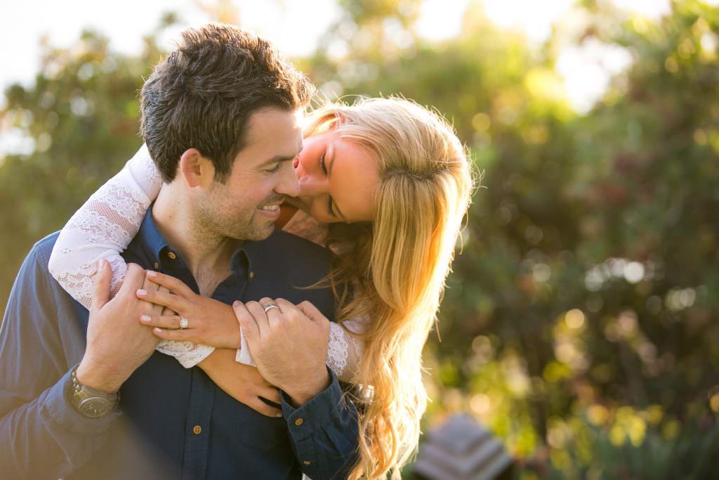 An engaged couple is posing for a picture in front of some trees in Huntington beach