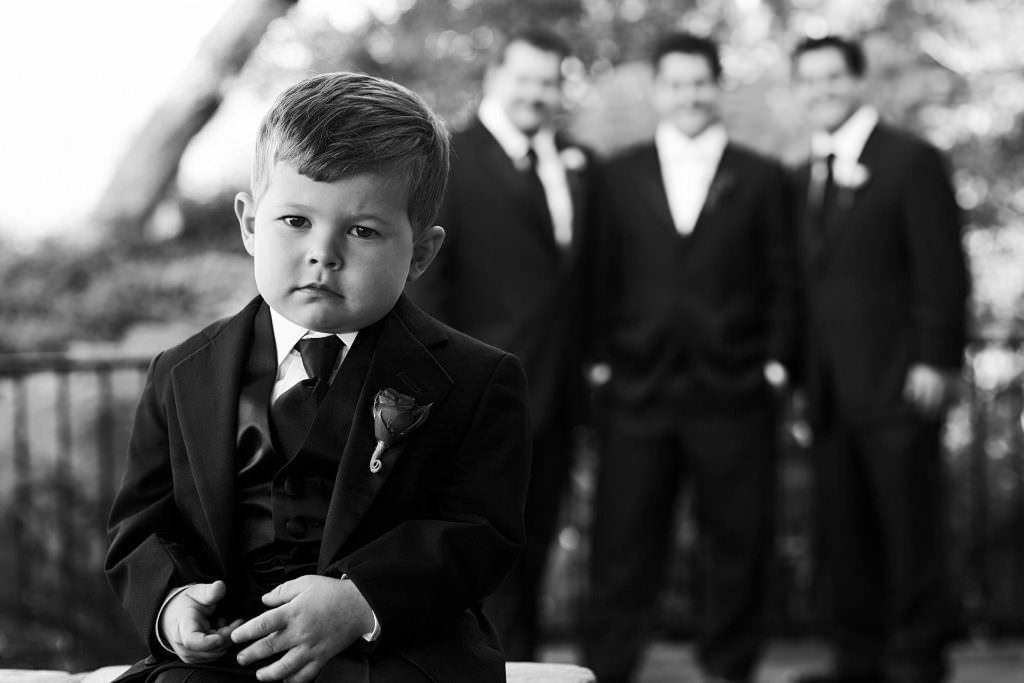 A little boy in a suit and tie is sitting in front of a group of men in suits.