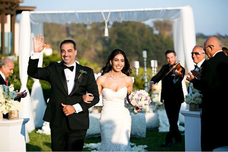 A bride and groom are walking down the aisle at their persian wedding