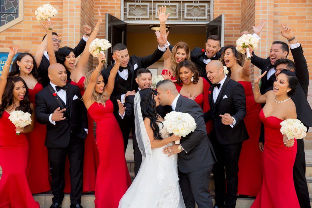 A bride and groom are kissing in front of their wedding party.