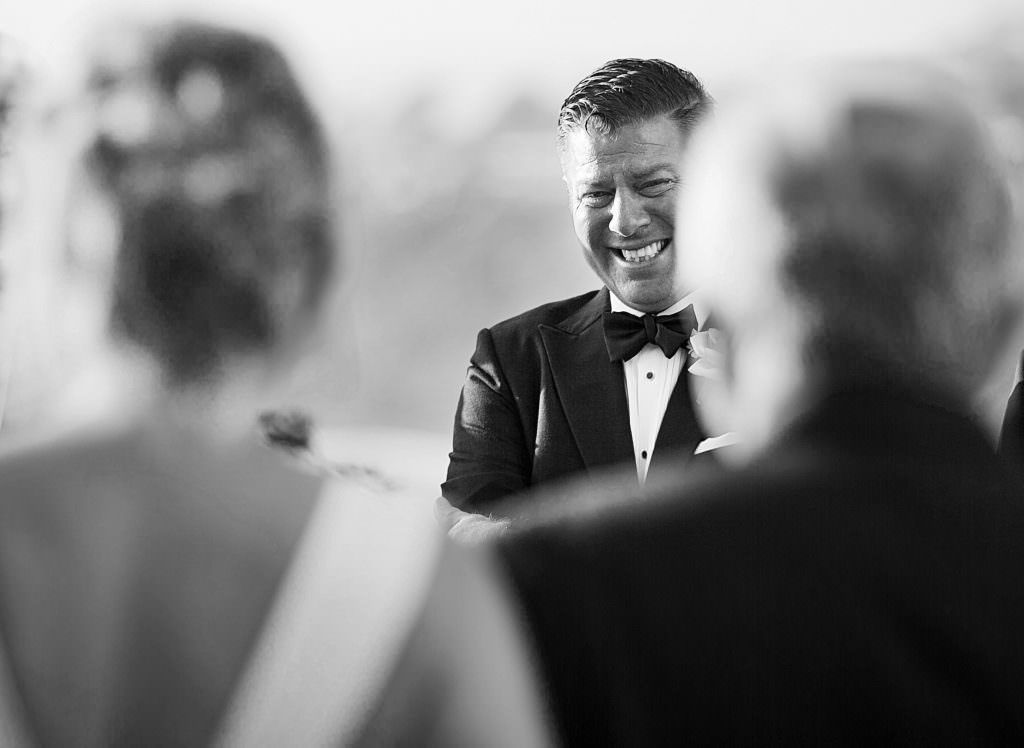 A man in a tuxedo is crying while his bride walks down the aisle towards him.