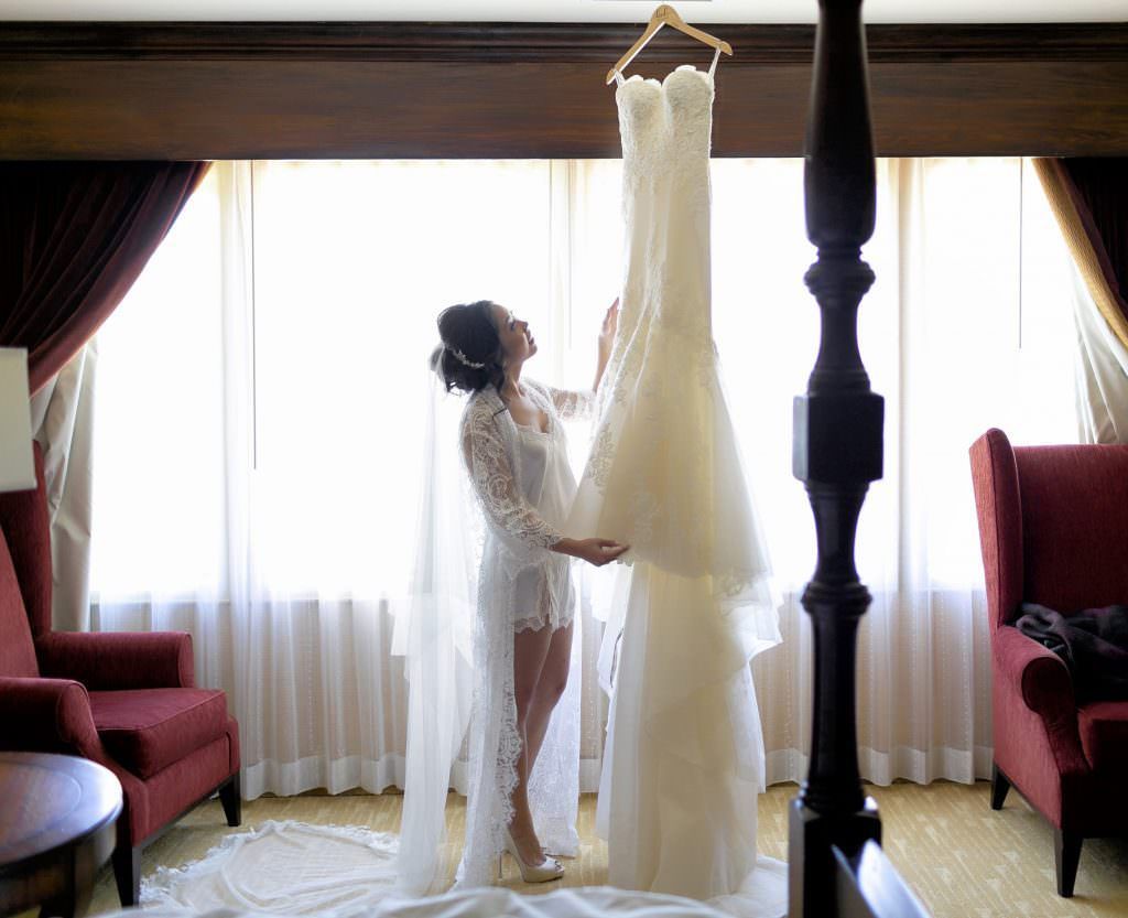 A bride is putting on her wedding dress in a hotel room.