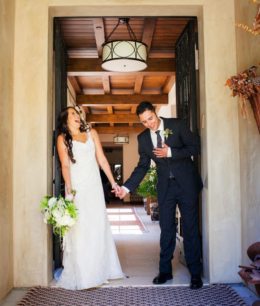A bride and groom are laughing during their first love in a doorway holding hands