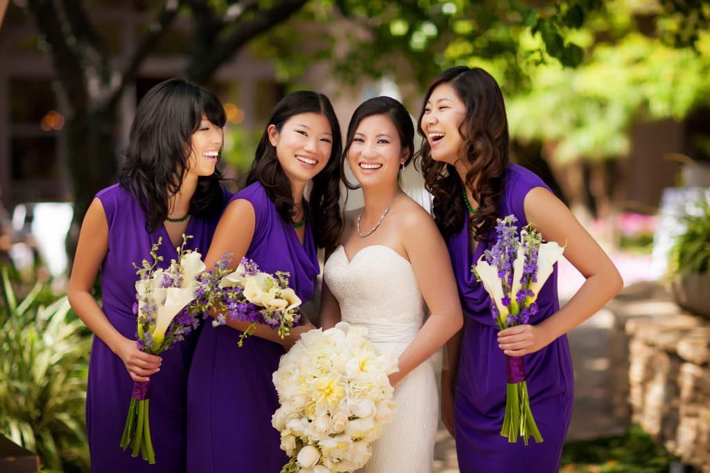 The bride and her bridesmaids are wearing purple dresses and holding bouquets of flowers.