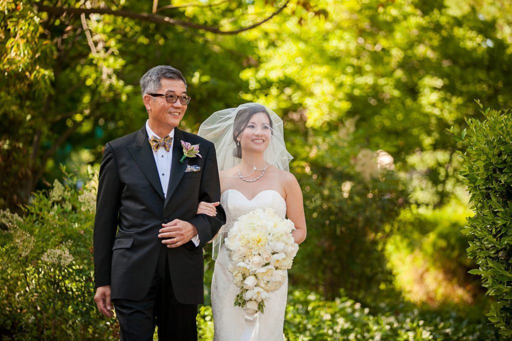 A bride and her father are walking down the aisle at their wedding.