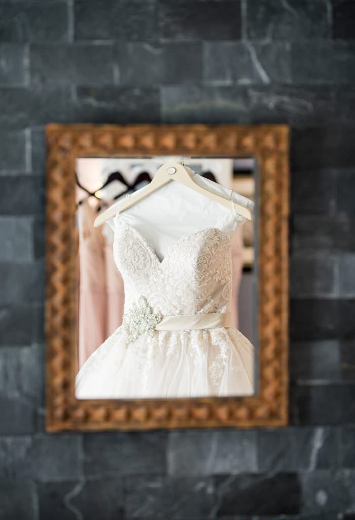 A wedding dress is hanging on a hanger in a mirror.