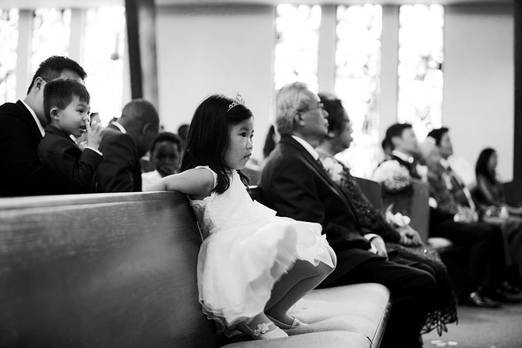 A little girl is sitting on a bench in a church watching a wedding ceremony.
