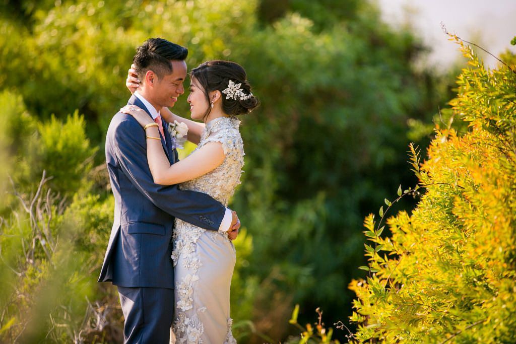 A Chinese bride and groom are posing for a picture in front of trees.
