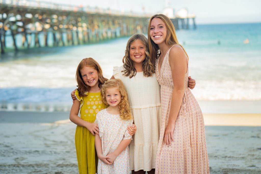 A group of four young sisters are posing for a picture on the beach.