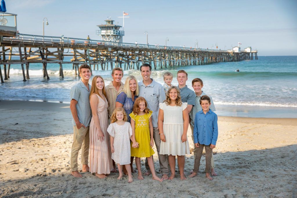 A large family is posing for a picture on the beach in front of the San Clemente pier.