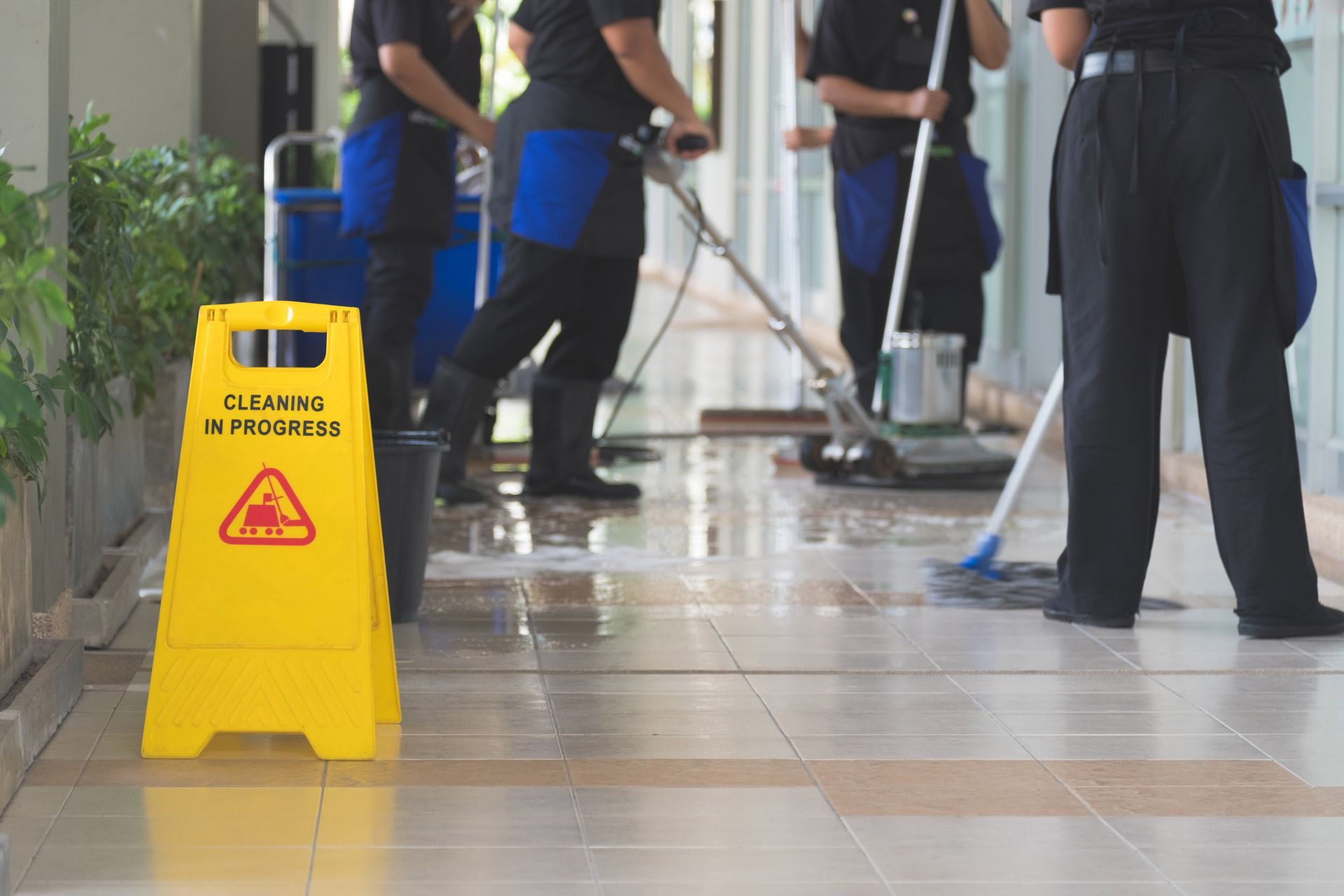Yellow caution sign in a hallway with cleaning crew workers mopping the floor.