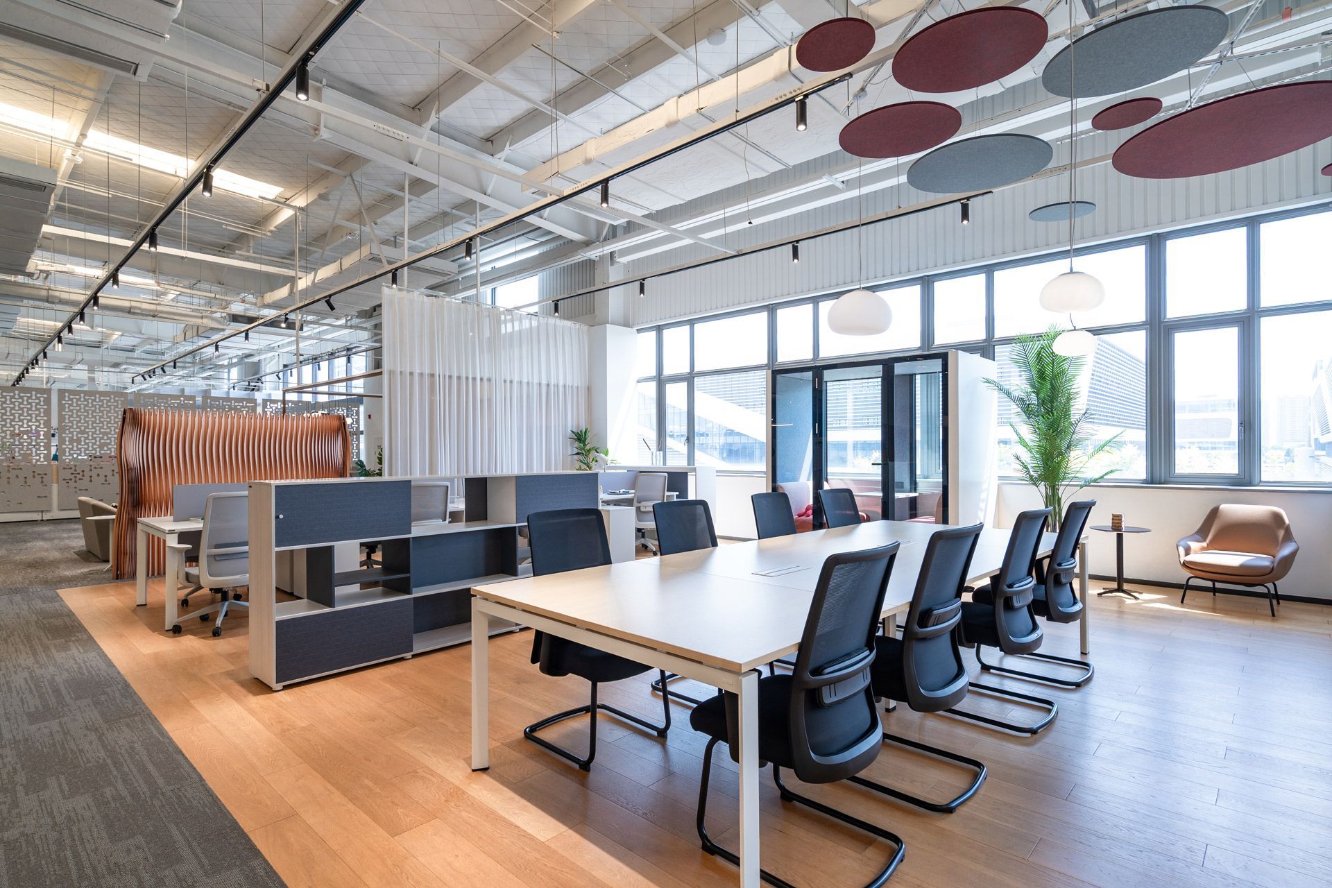 Modern office interior featuring a light wood conference table, black chairs, open workstations, and decorative ceiling discs.