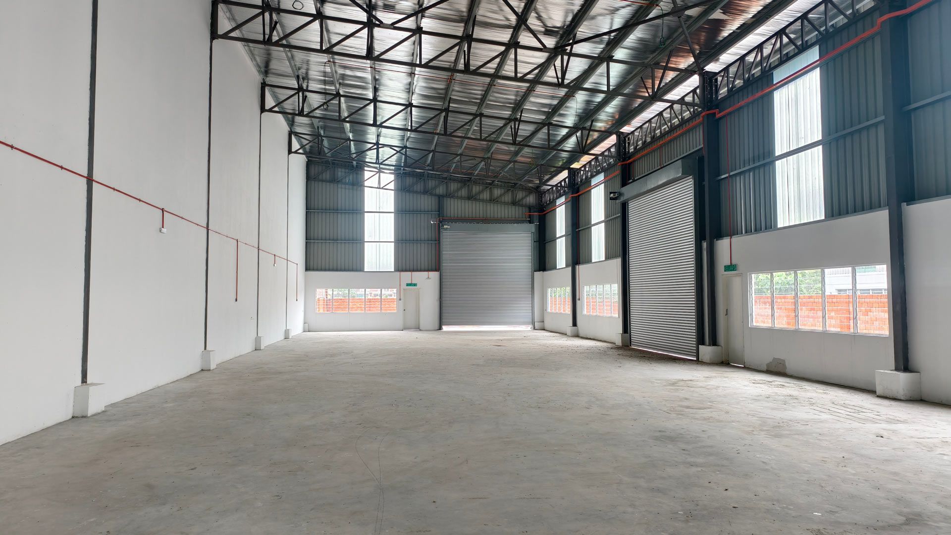 An empty, spacious industrial warehouse with high metal ceilings, white walls, and large roll-up doors.