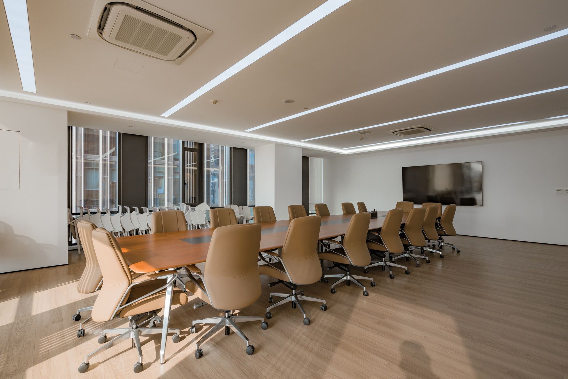 A long wooden conference table with tan chairs in a bright, modern, minimalist office space.