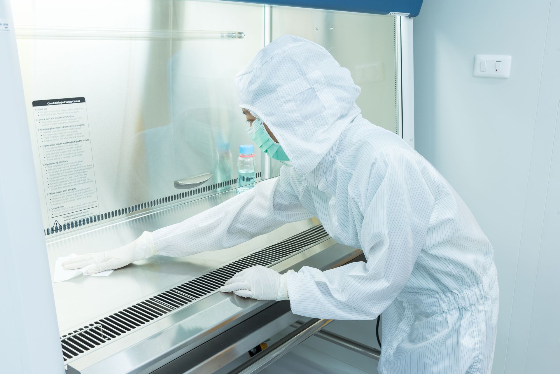Person in a white protective suit cleans a laboratory hood.