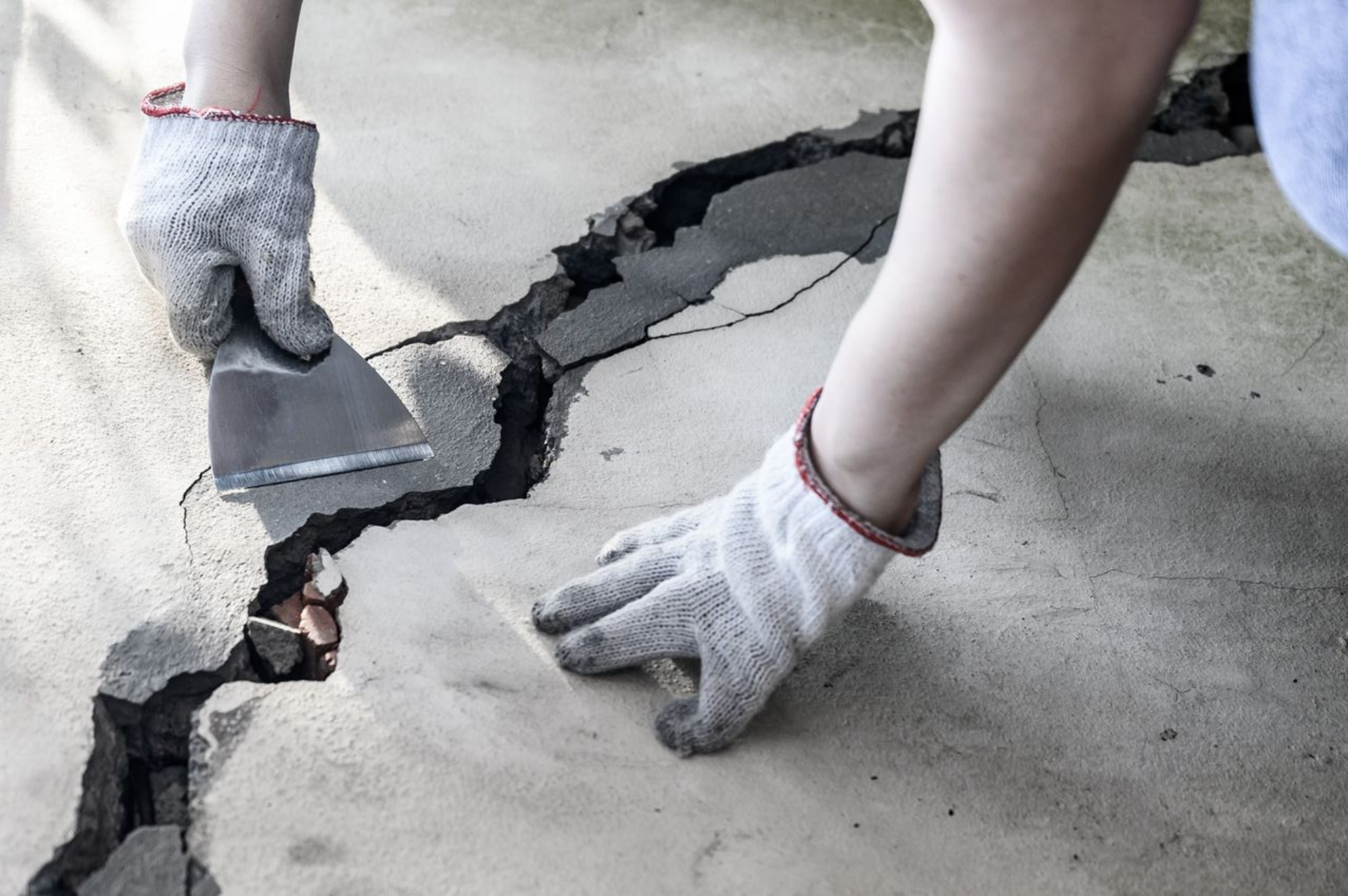 Person patching a cracked concrete floor with a trowel, wearing gloves.