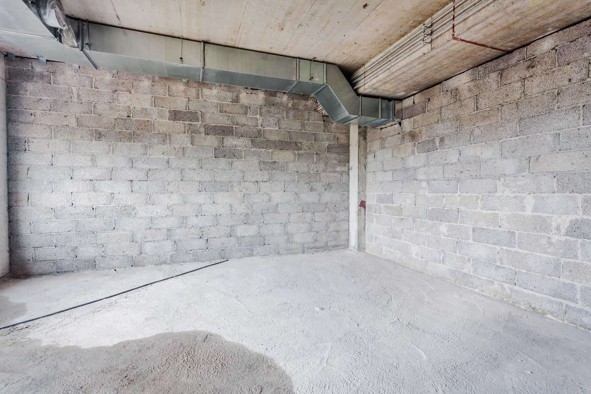 An unfinished interior space with raw concrete block walls, a concrete ceiling, and exposed metal ventilation ductwork.